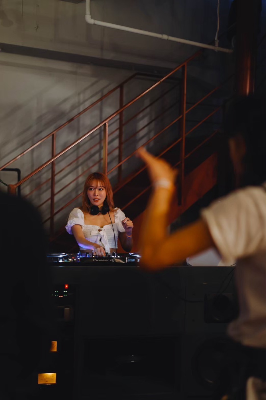 階段のある会場。DJ卓の奥にDJが立ち、手前で客が手を上げている