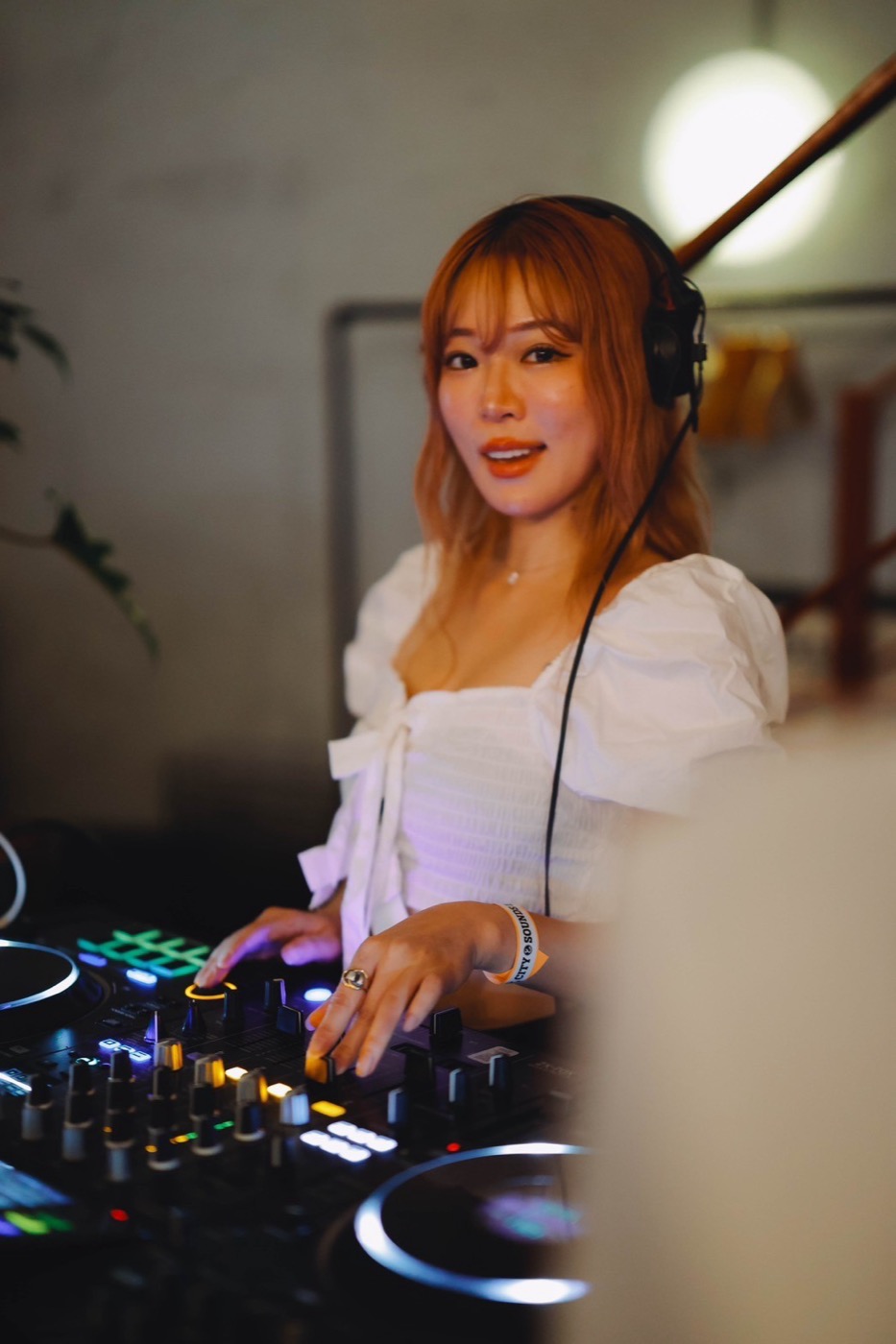 屋内でDJコントローラーを操作する人。ヘッドフォンをつけてこちらを見ている