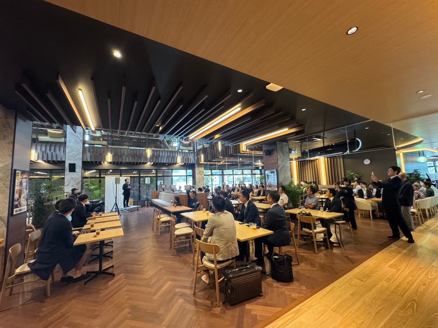 スタンドマイクで話す司会と、着席した参加者