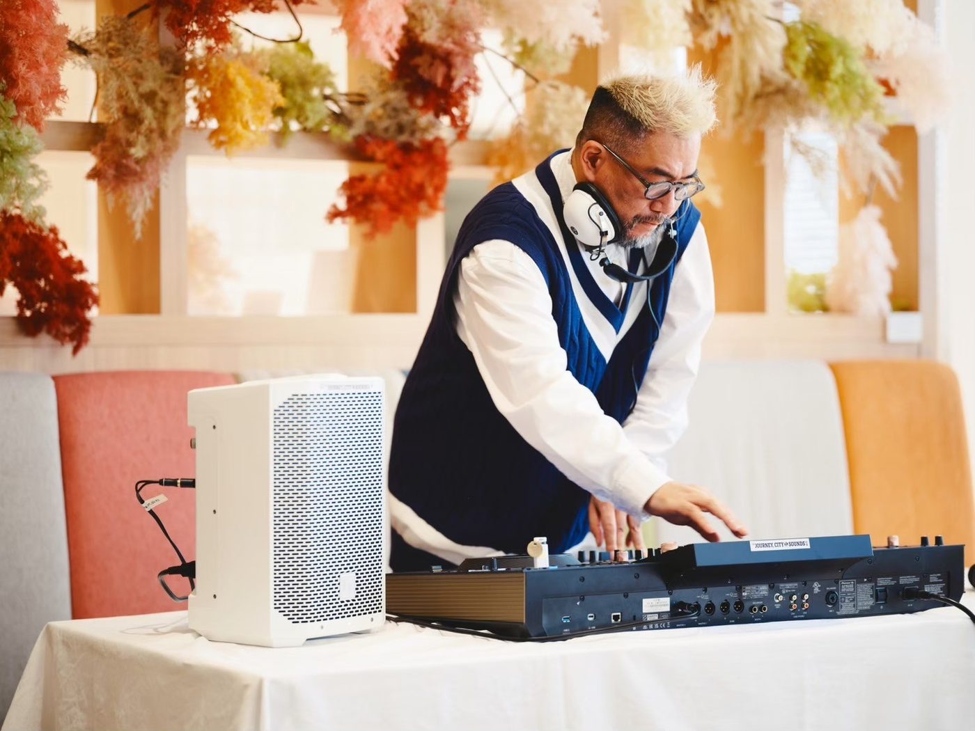 レストランのテーブルに置いたDJコントローラーとスピーカー1本。その前にDJが立っている