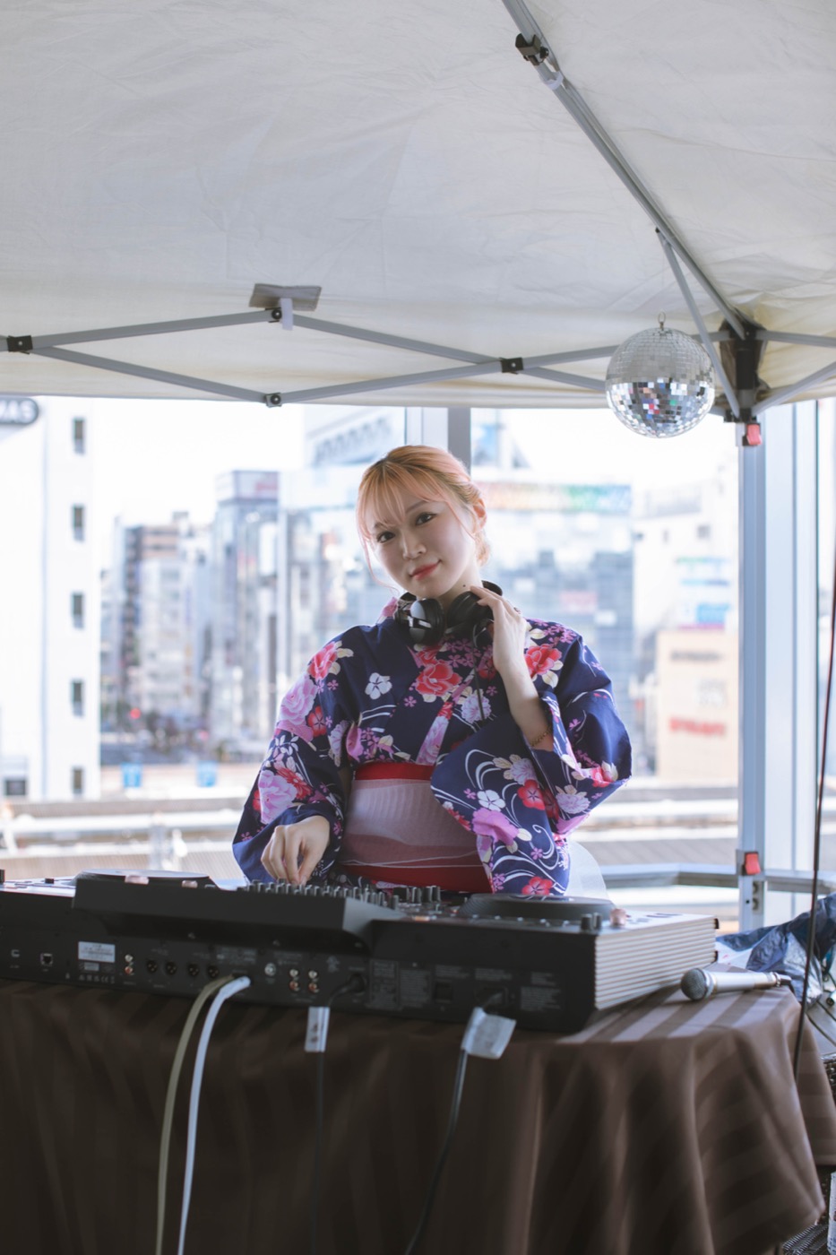 ビルの屋上。テントの下のDJ卓に立ち、首にヘッドフォンをかけている